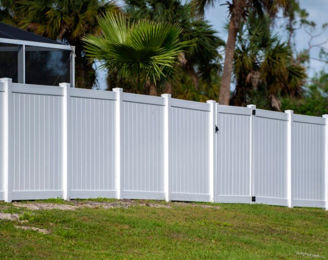 White vinyl picket fence on green lawn surrounding property grounds for backyard protection and privacy.