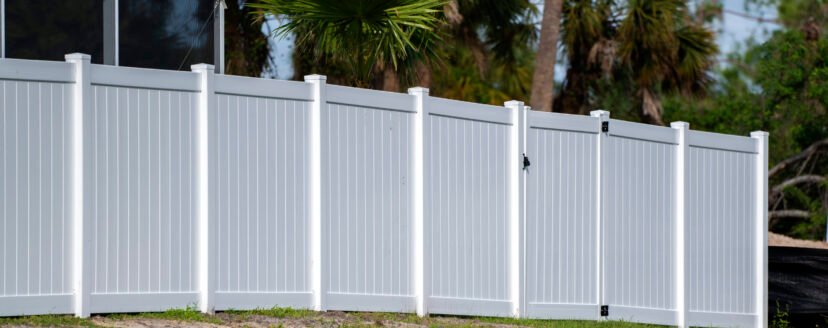 White vinyl picket fence on green lawn surrounding property grounds for backyard protection and privacy.