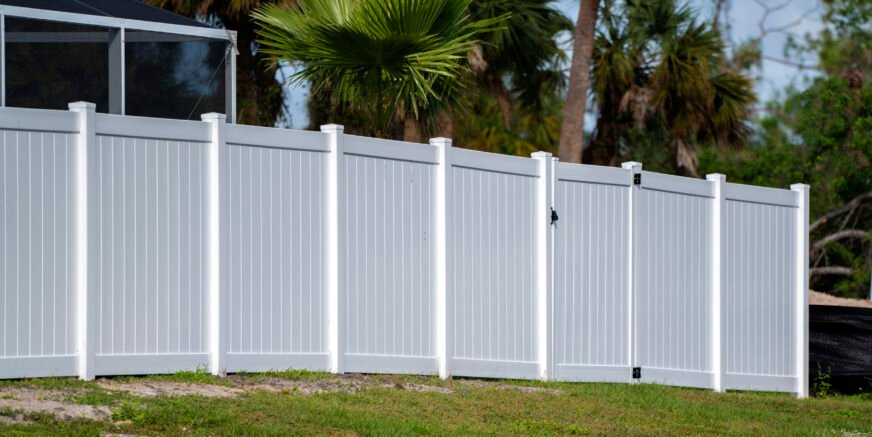 White vinyl picket fence on green lawn surrounding property grounds for backyard protection and privacy.
