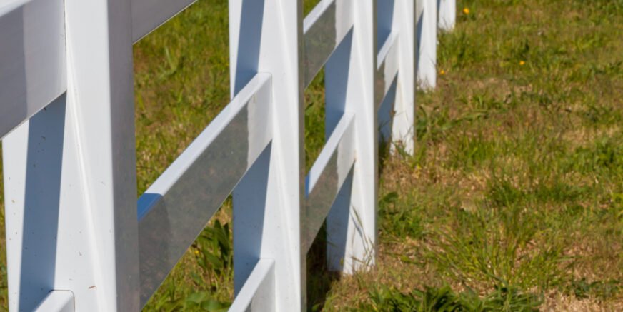 Country New White Plastic Fence after Mowing. Sunny day