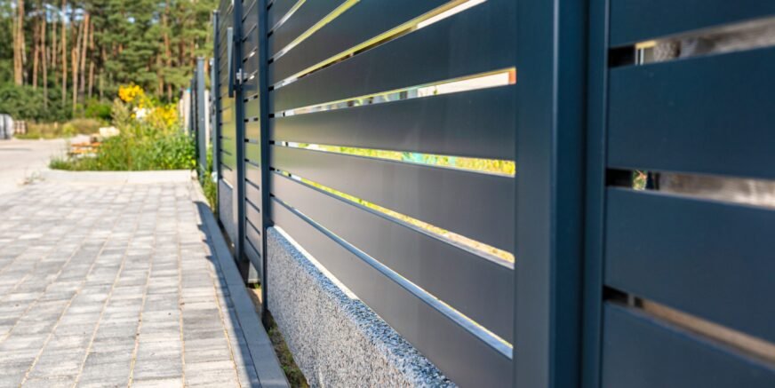 Modern panel fencing in anthracite color, visible spans and a wicket, forest in the background.